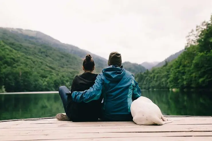 minimalist couple with dog sitting in front a lake